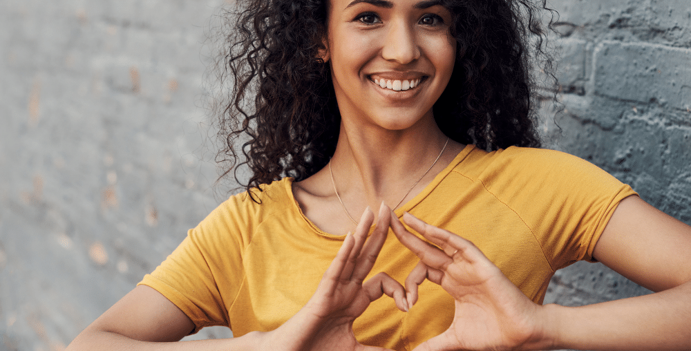 Woman in gold shirt making heart with hands