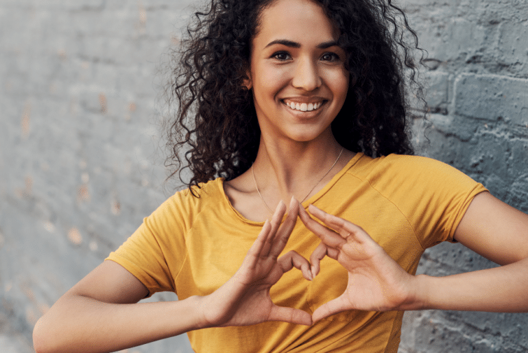 Woman in gold shirt making heart with hands