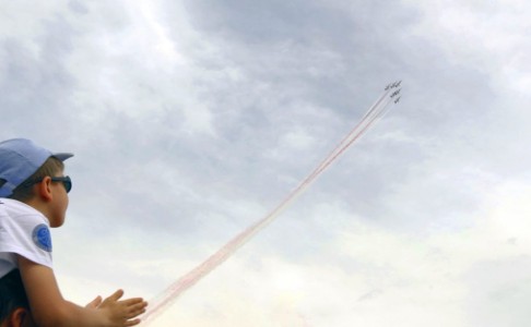 A kid looking up at the sky as a group of fighter pilots fly above him 