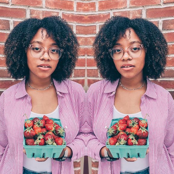 Teen influencer girl holding strawberries in front of a brick wall