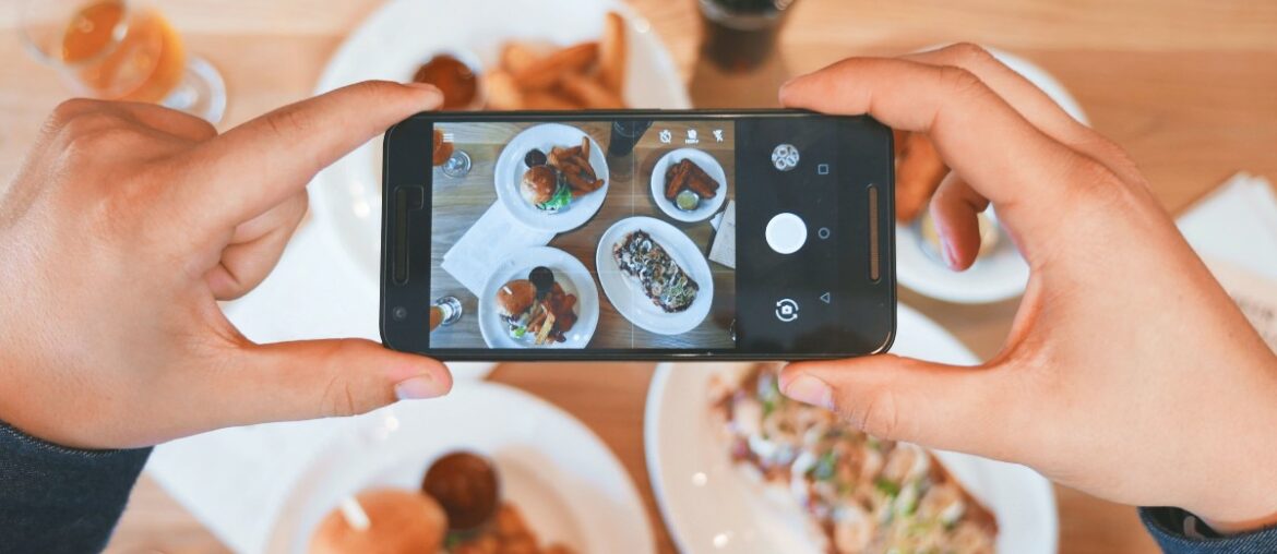 A close-up of a person taking pictures of their food with the food in the background.