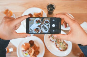 A close-up of a person taking pictures of their food with the food in the background.