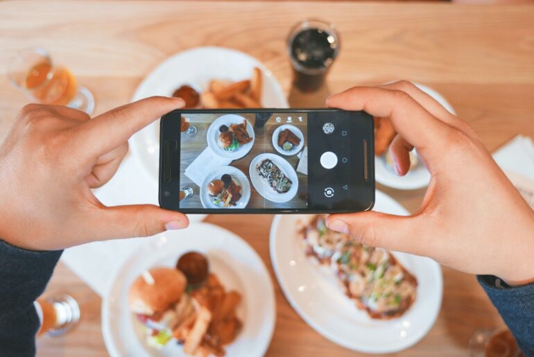 A close-up of a person taking pictures of their food with the food in the background.