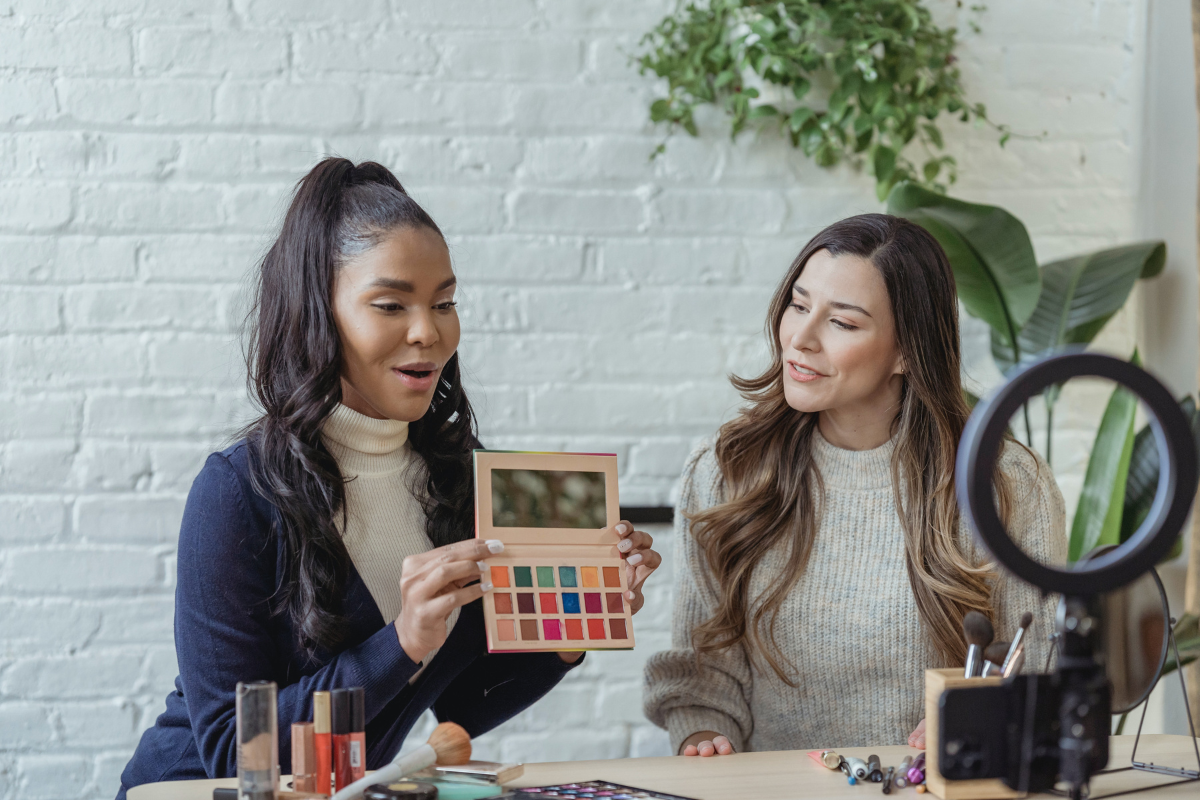 Two women talking to a camera as they show off makeup products