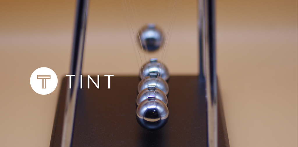 Marble Impact on Newton's Cradle next to TINT logo