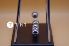 Marble Impact on Newton's Cradle next to TINT logo