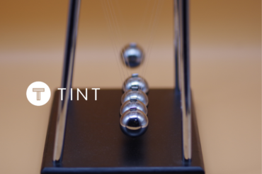 Marble Impact on Newton's Cradle next to TINT logo