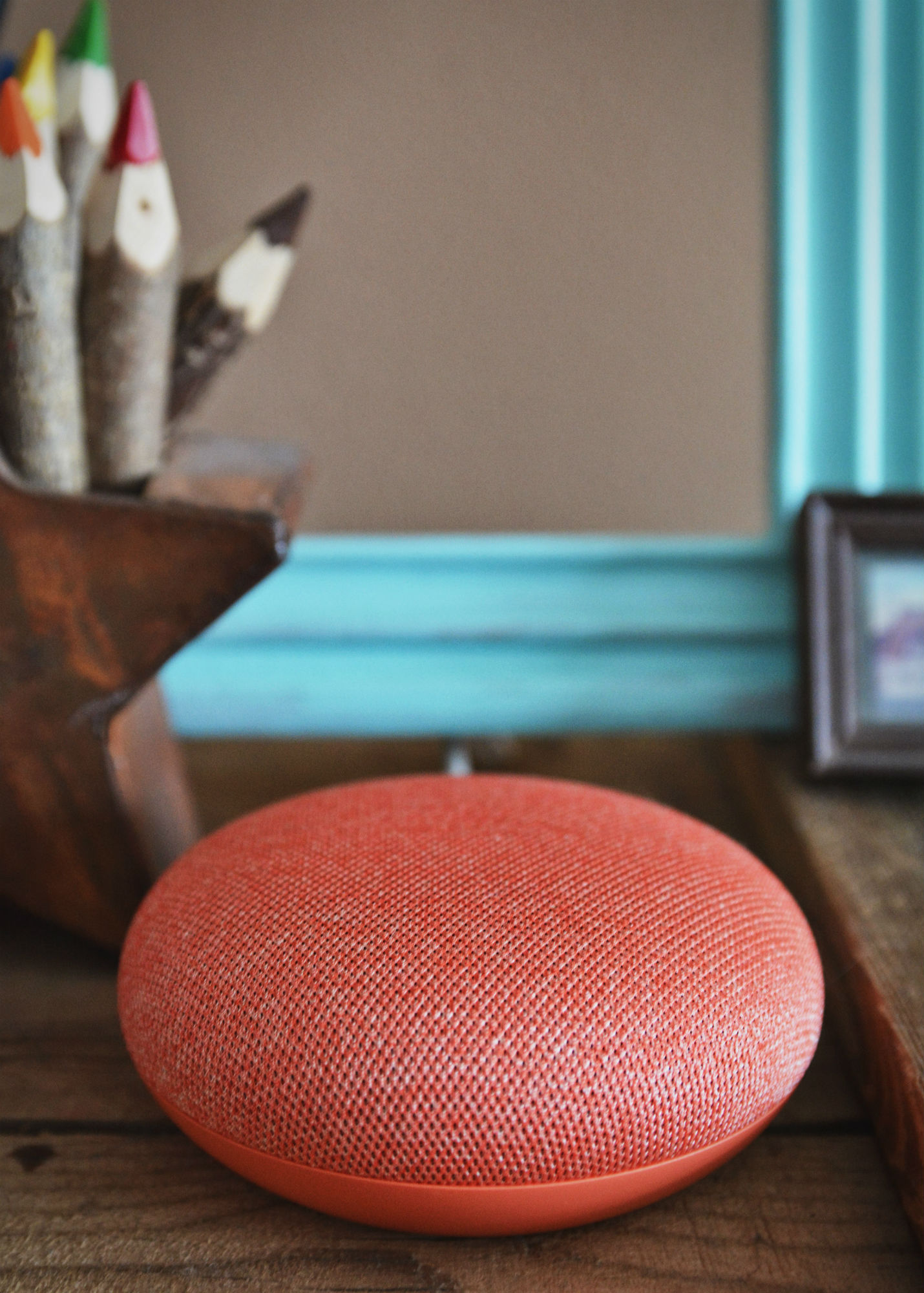 Red Google home search smart speaker on a desk in front of pencils