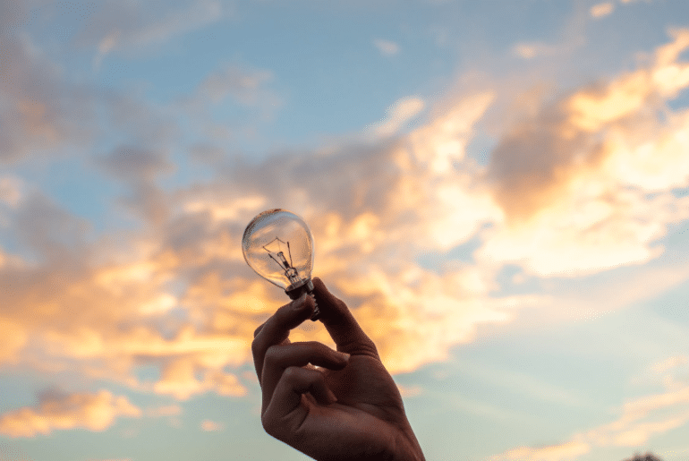 A person holding a lightbulb towards the sky