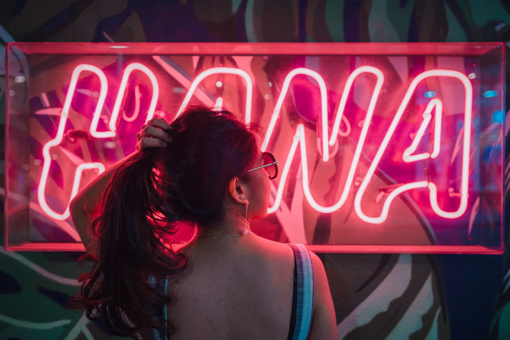 Gen Z girl wearing sunglasses in front of neon sign
