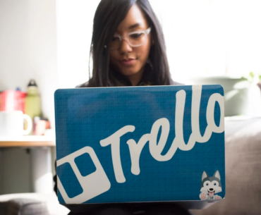 A woman on her laptop with a sticker that says Trello