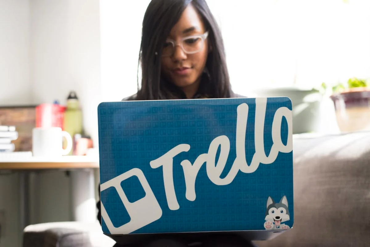 A woman on her laptop with a sticker that says Trello
