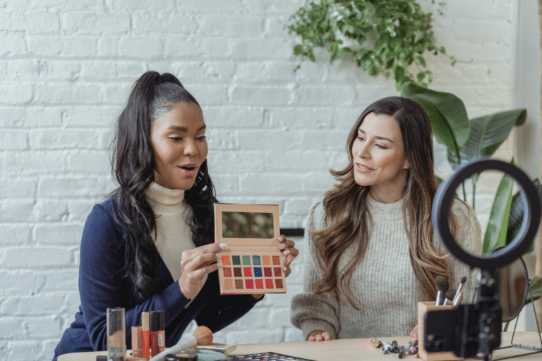 Two women showing makeup products to the camera