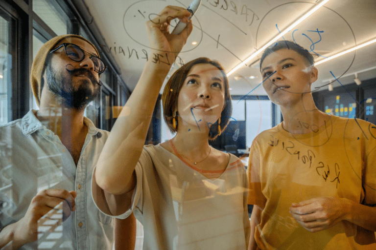 Three people writing on a see-through whiteboard