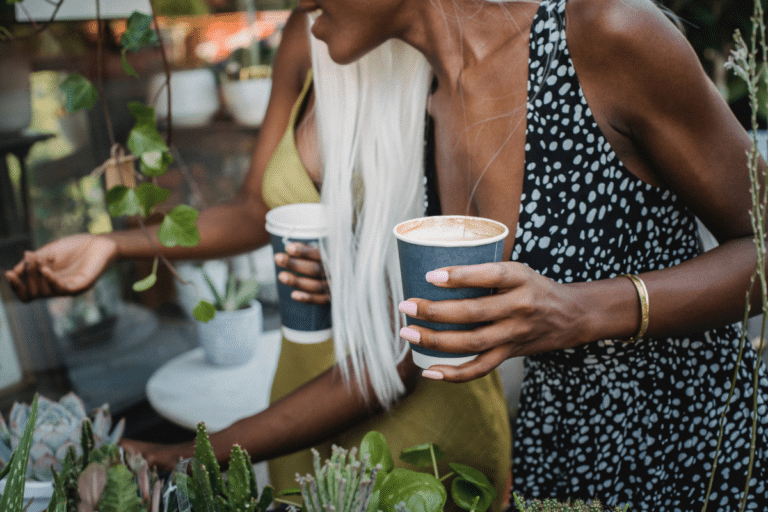 Two women shopping for plants as they hold coffee