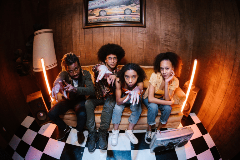 Four young people sitting on a couch, pointing at the camera