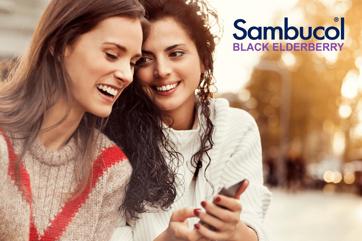 Two women looking at a mobile phone alongside the Sambucol logo